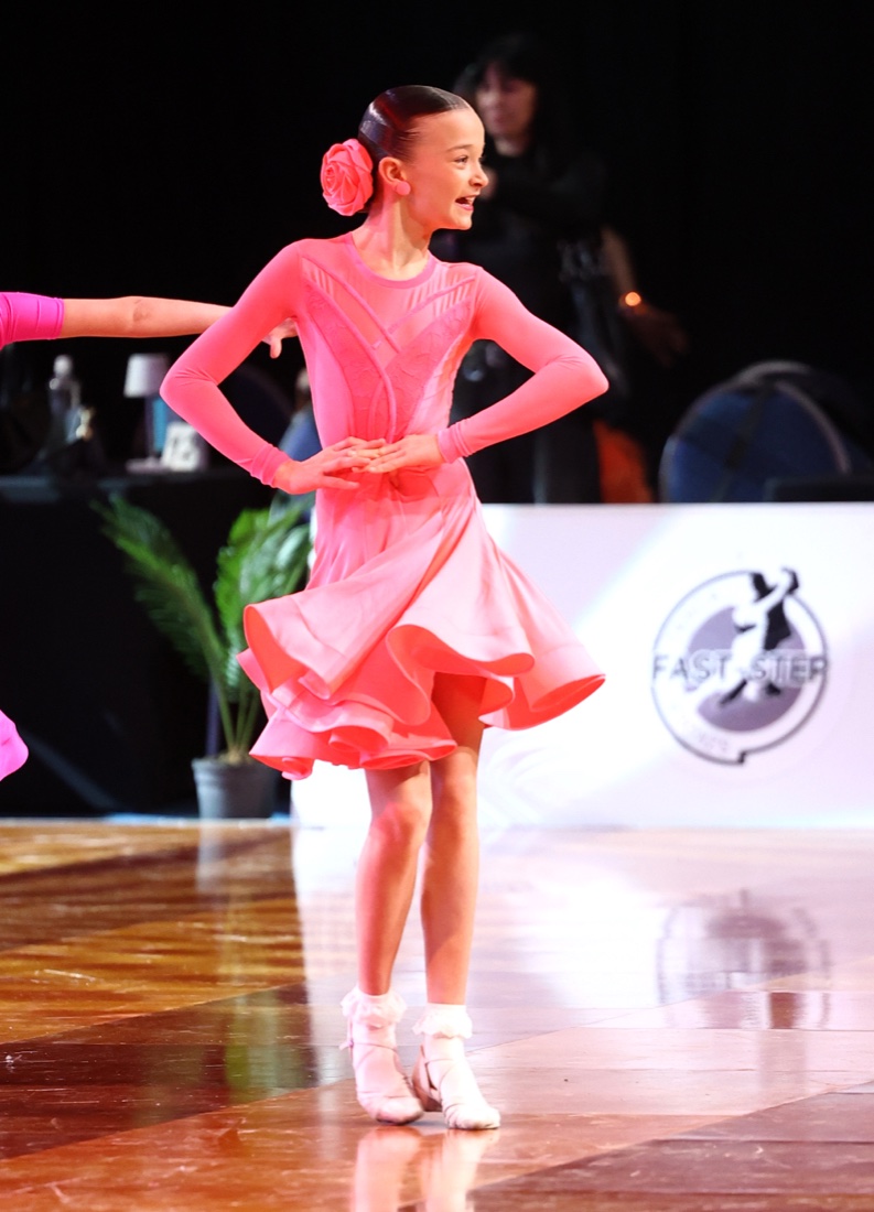 Młoda tancerka Dance Factory w figurze na parkiecie turniejowym